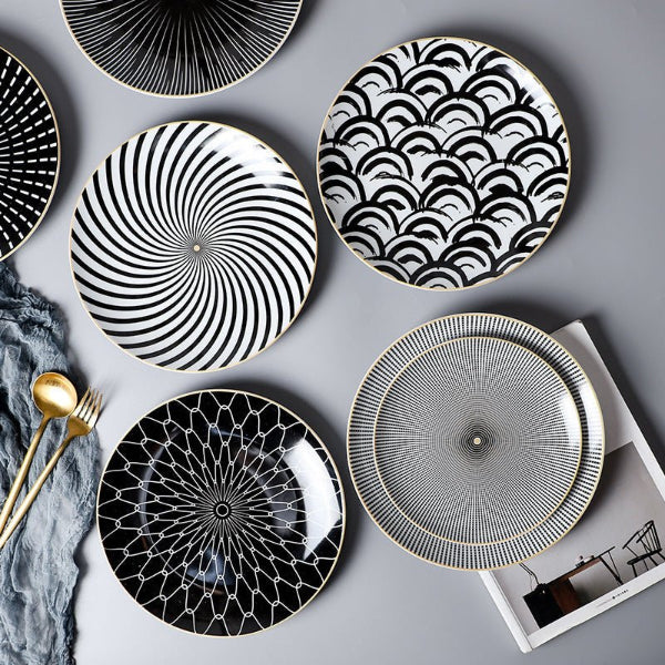 Set of black and white patterned plates on a gray surface with gold cutlery.