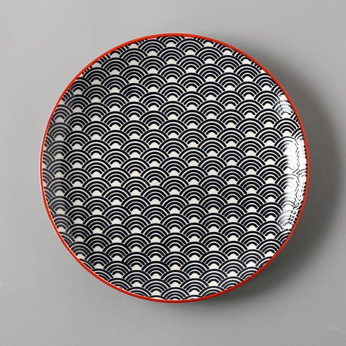 Round plate with black wave pattern and red rim on a gray background
