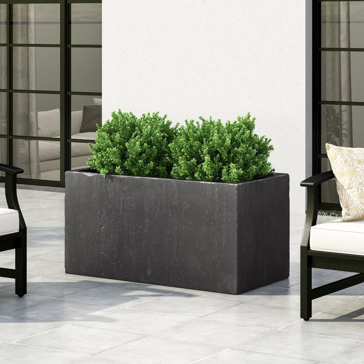 Rectangular black planter with green plants on a patio with chairs and a couch.