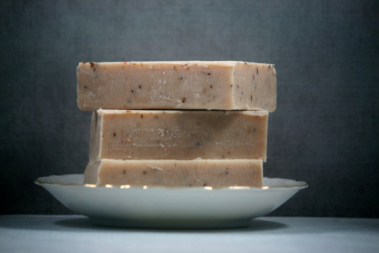 Three bars of soap stacked on a white plate against a dark background