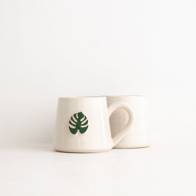 Black Oak Art Monstera Mug showing front and back views with tropical monstera leaf designs on ceramic coffee mug.