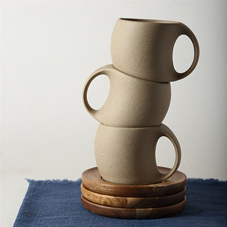 Stack of three beige ceramic mugs on a wooden coaster with a blue cloth background