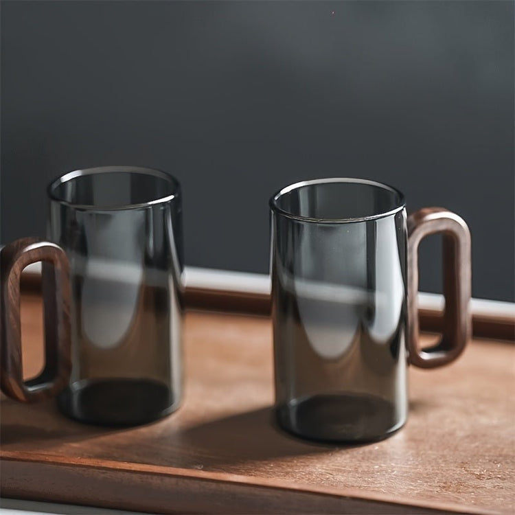 Two clear glass mugs with wooden handles on a wooden tray against a dark background