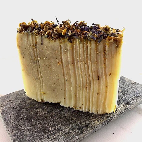 Bar of soap with dried herbs on a dark stone surface