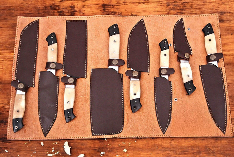 Handmade Damascus kitchen knives set with sharp blades and intricate pattern, displayed on a wooden countertop.