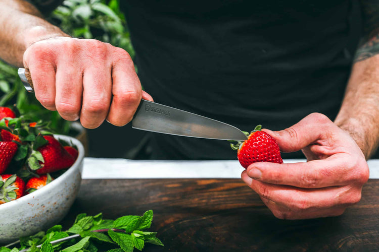 Steelport Knife Co. 4-inch paring knife slicing a strawberry, showcasing its sharp blade and ergonomic handle for precise kitchen tasks.