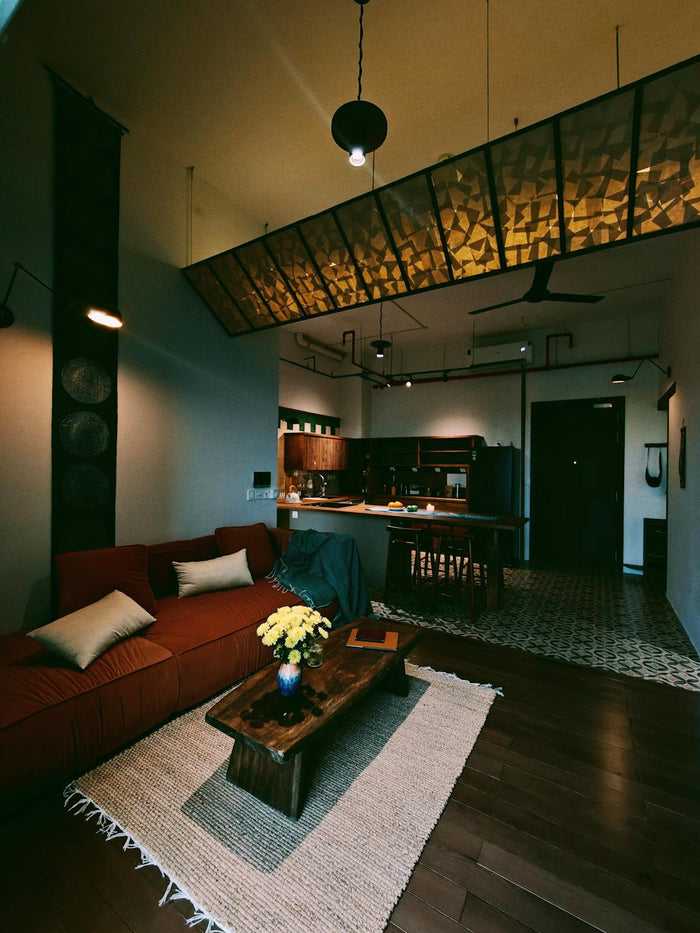 Modern minimalist living room with light gray sectional sofa, black armchair, wood beam ceiling, and large white coffee table with greenery centerpiece.