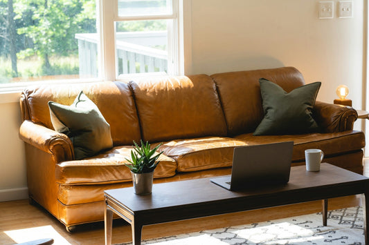 Warm living room with brown leather sofa, wooden coffee table, and natural light from large windows