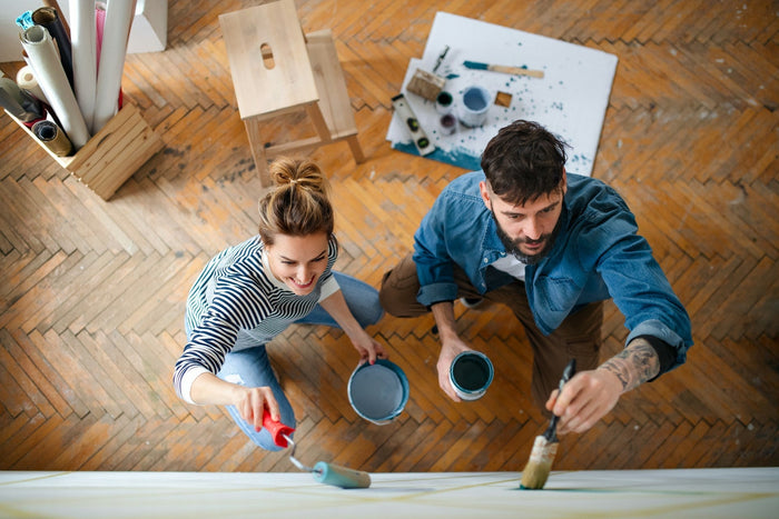 Couple painting walls together during a home renovation project on herringbone parquet flooring