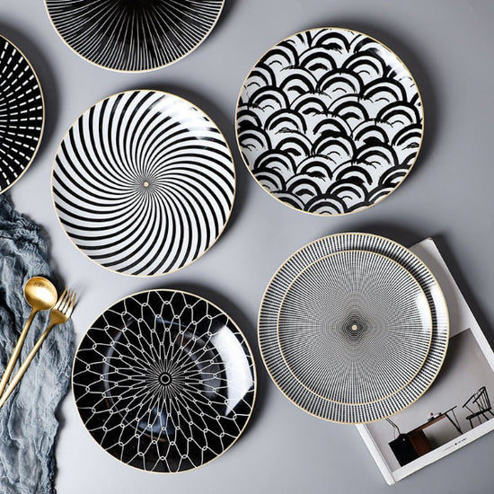 Set of black and white patterned plates on a gray surface with gold cutlery.