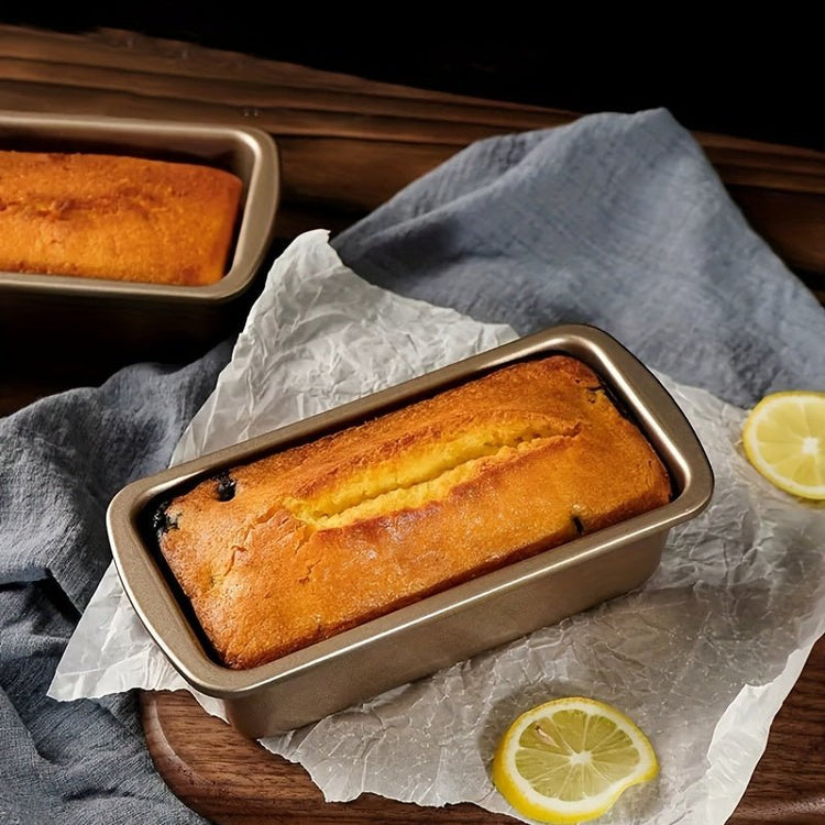 Loaf of bread in a baking pan on a wooden surface with lemon slices.
