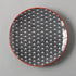 Round plate with black wave pattern and red rim on a gray background