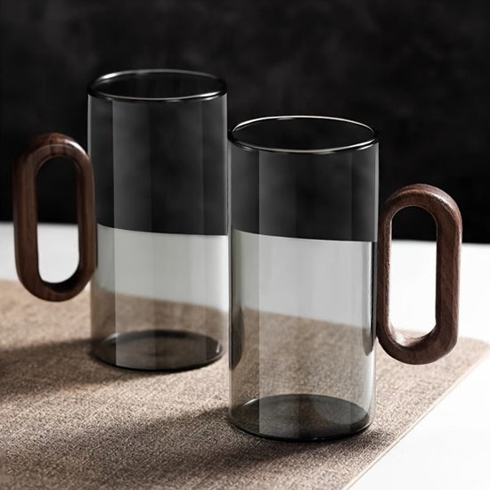Two glass mugs with wooden handles on a textured surface.