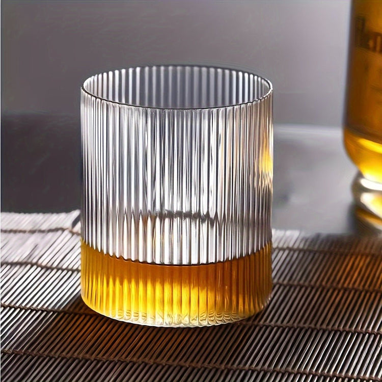 Clear glass tumbler with ribbed design filled with a yellowish liquid on a textured surface.