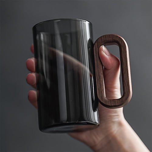 Black mug with a wooden handle held by a hand against a dark background