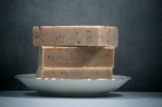 Three bars of soap stacked on a white plate against a dark background