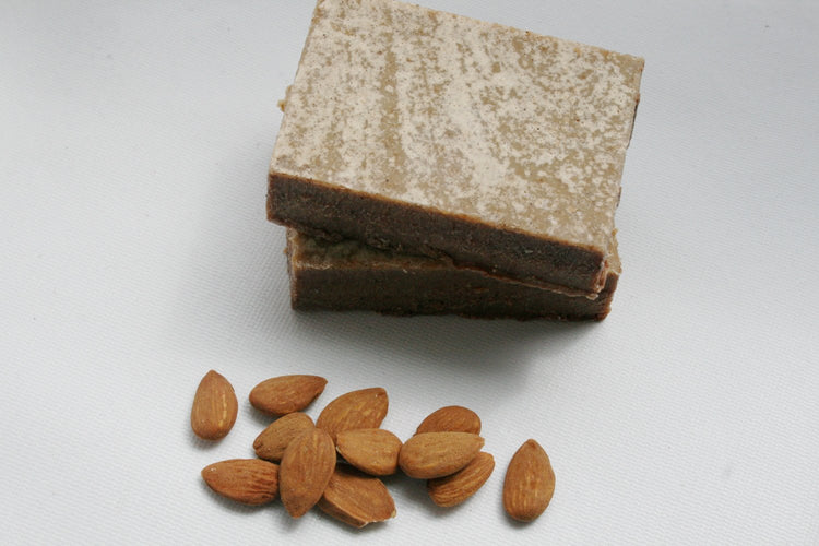 Two pieces of brown almond butter on a white background with almonds scattered around.