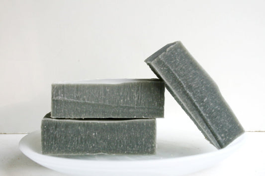 Three bars of dark soap stacked on a white plate with a white background