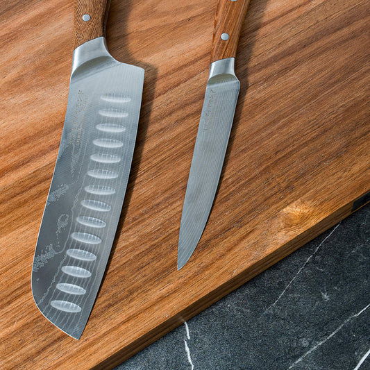Swiss Diamond Damascus Santoku and paring knife set with matching blades and handles, displayed on a wooden surface.