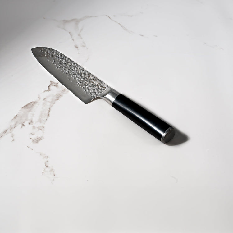 Swiss Diamond 7-inch hammered Santoku knife with a white marble-patterned handle, showcasing its sharp blade and textured surface.