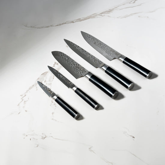 Swiss Diamond hammered 5-piece knife set with white marble handles, displayed on a white marble surface.