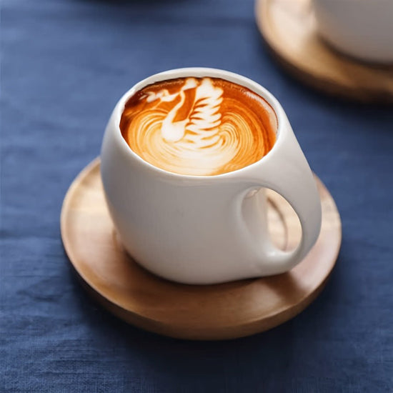 White ceramic cup with a latte art design on a wooden coaster against a blue background