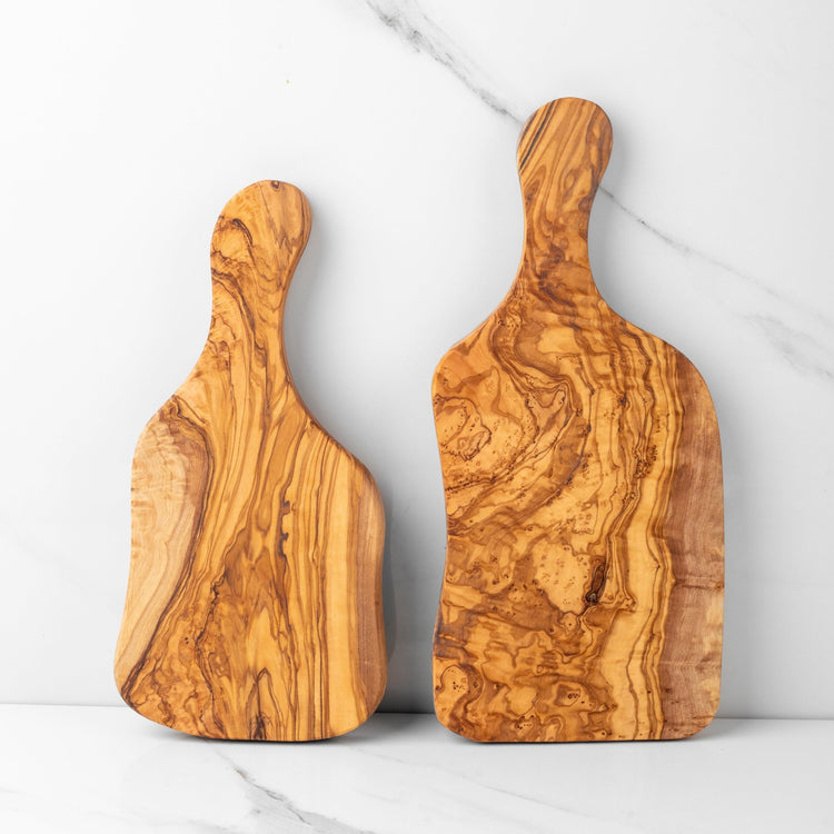 Two wooden cutting boards with handles on a marble surface