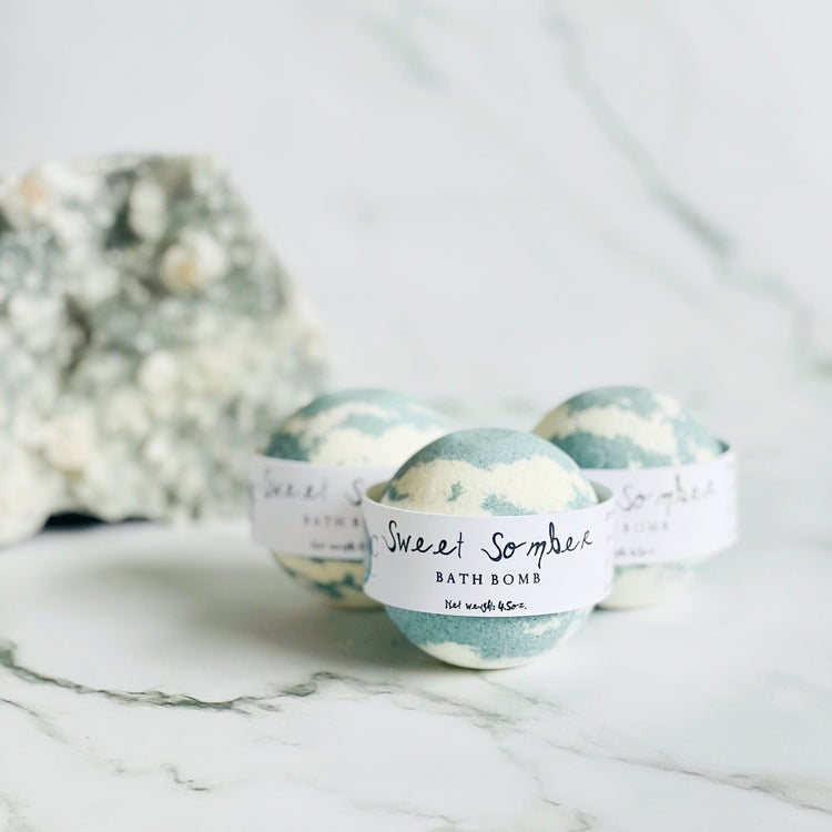 Three bath bombs labeled 'Sweet Summer' on a marble surface with a blurred floral background.