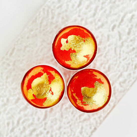 Three red and gold spherical objects on a textured white surface