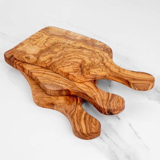 Two wooden cutting boards with handles on a white marble surface