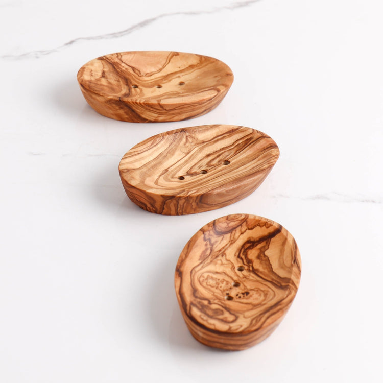 Three wooden soap dishes with a marbled pattern on a white marble surface