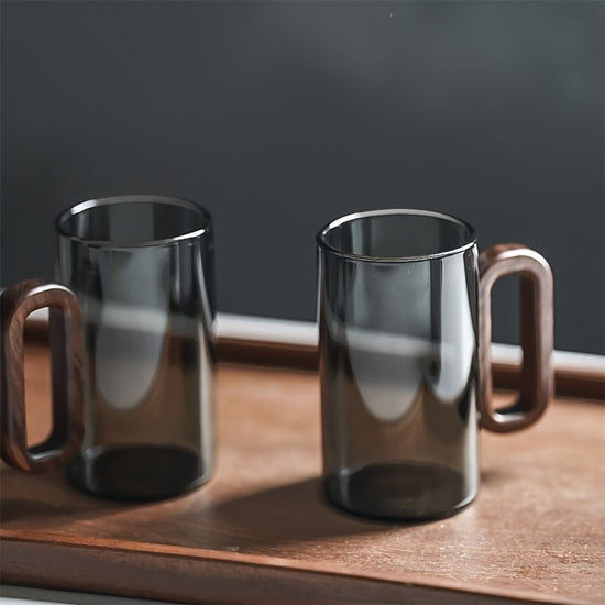 Two clear glass mugs with wooden handles on a wooden tray against a dark background