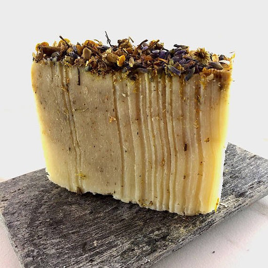 Bar of soap with dried herbs on a dark stone surface