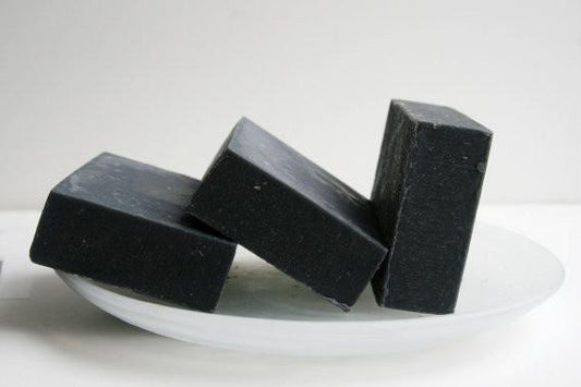 Three pieces of black soap on a white plate with a white background